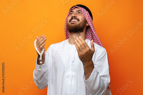 Photography Young Arab man holding traditional beads against orange background