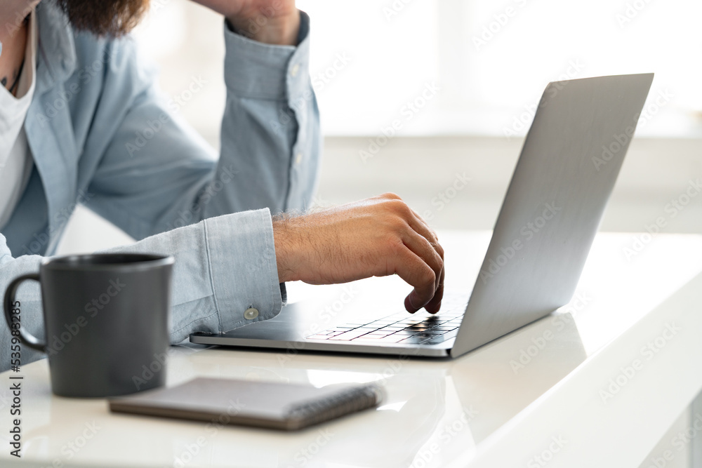 Close up shot of a man sitting at the table and working on laptop at home Close up shot of a man sitting at the table and working on laptop at home