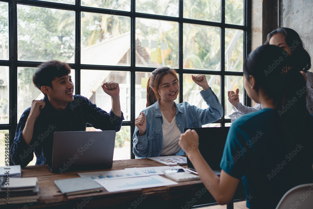 Group of creative young Asian business people happy, successful work, accomplished goals. Excited. Raise your hand to congratulate your colleagues in the office.