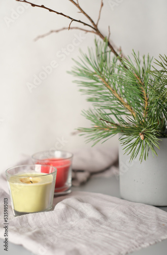 glowing candles on linen textile next to cement vase with pine tree branch. aesthetic composition home decor and cozy ambience. vertical