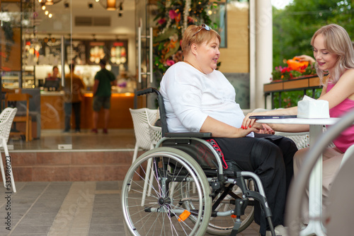 Woman with disability sitting in a wheelchair in outdoor cafe with her young daughter