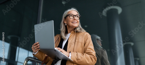 Fotografie Business senior woman working on a laptop online against the backdrop of an offi