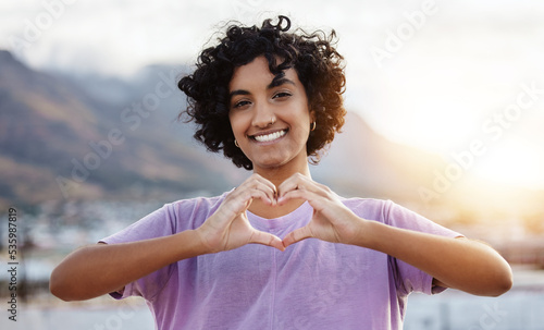 Hand, heart and woman showing love sign in a city, travel, freedom and happy student. Portrait, smile and finger gesture with cheerful indian tourist enjoying foreign exchange programme in Mexico photo