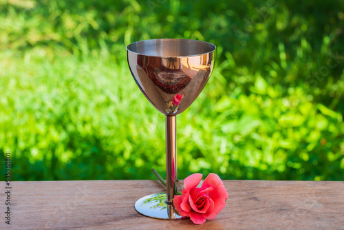 Silver shot glass and red rose on a wooden table in the garden