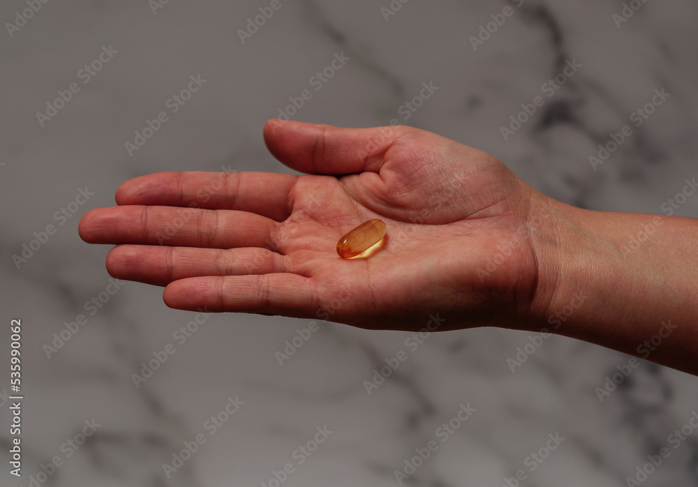 Capsule of Omega-3 on palm. Marble background. Horizontal view. Focus on capsule Capsule of Omega-3 on palm. Marble background. Horizontal view. Focus on capsule