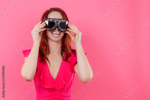Portrait of Smiling Happy Young Caucasian Woman in Spectacles Wearing Bright Red Dress Over Pink Background.