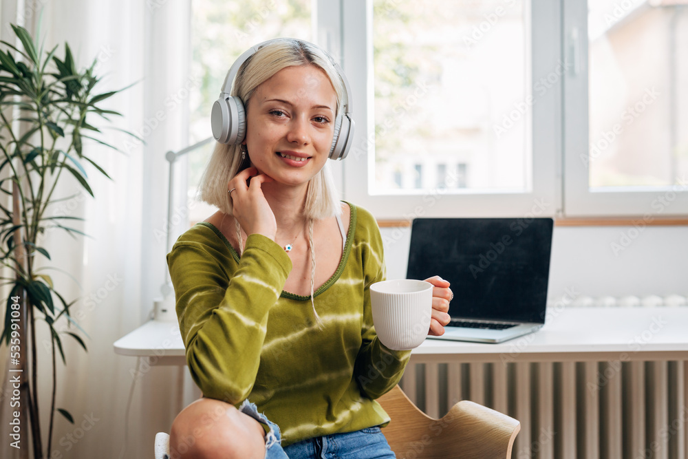 woman with headphones drinking coffee and looking at camera while sits in her room woman with headphones drinking coffee and looking at camera while sits in her room