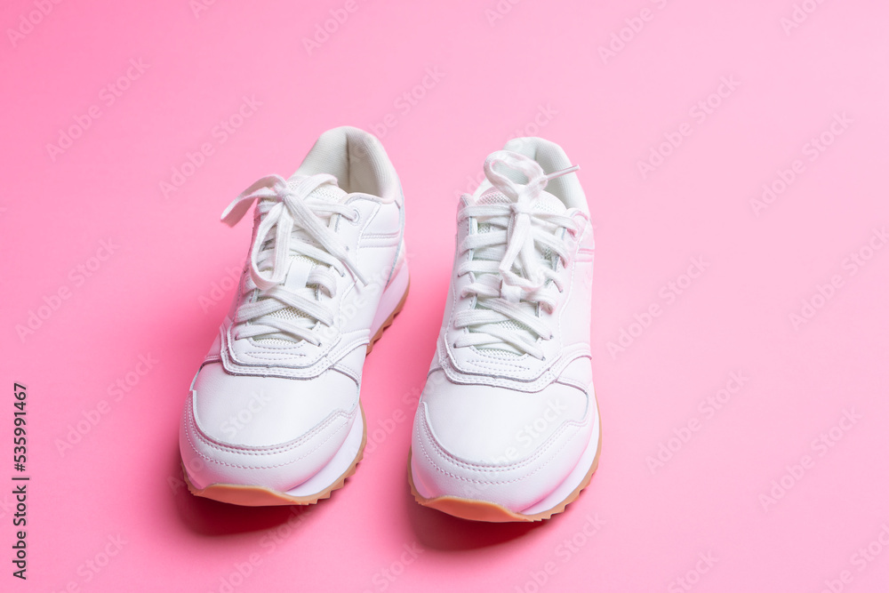 Pair of New White Sneakers Over Pink Seamless Background.