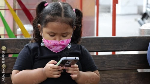 Asian little girl sitting while playing cellular phone or smartphone or gadget in public space photo