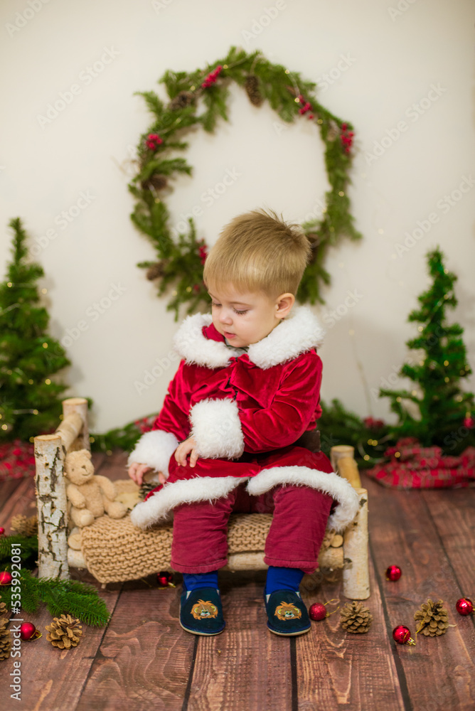 Little cute boy dressed as Santa Claus in a room decorated for Christmas. Christmas and children