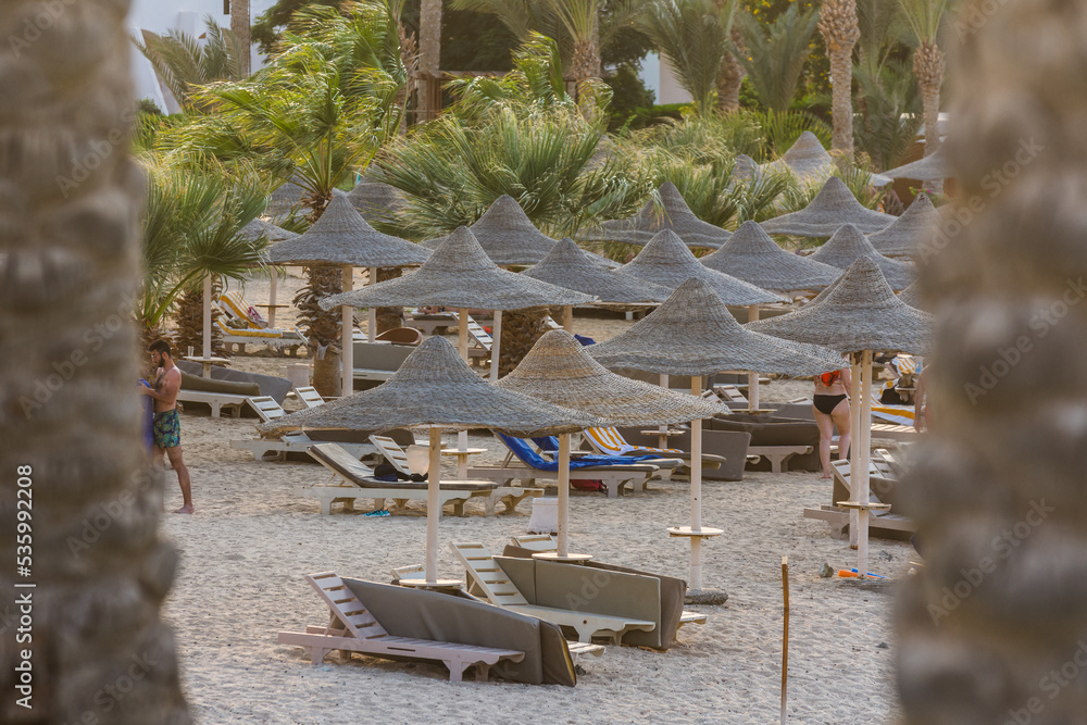 Obraz premium view through palm trees to many beach umbrellas at the sea