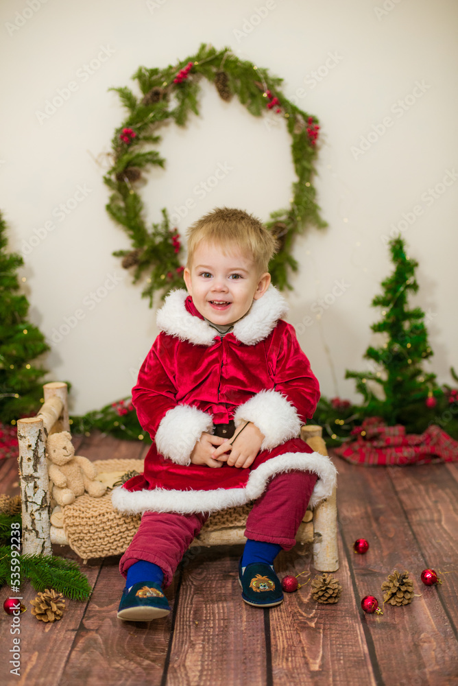 Little cute boy dressed as Santa Claus in a room decorated for Christmas. Christmas and children