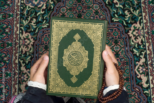 The Koran is held by a woman on a prayer rug photo