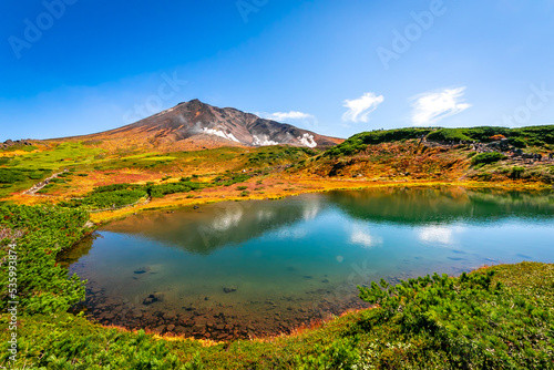 秋の北海道・大雪山の旭岳で見た、池の周りを彩る紅葉や緑の植物と快晴の青空 © 和紀 神谷
