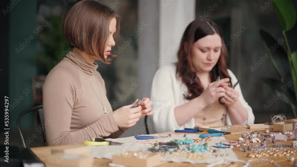 Two jewelry designers working in studio with tools making gemstone necklaces, bracelets and earrings. Female friends crafting jewellery together Two jewelry designers working in studio with tools making gemstone necklaces, bracelets and earrings. Female friends crafting jewellery together