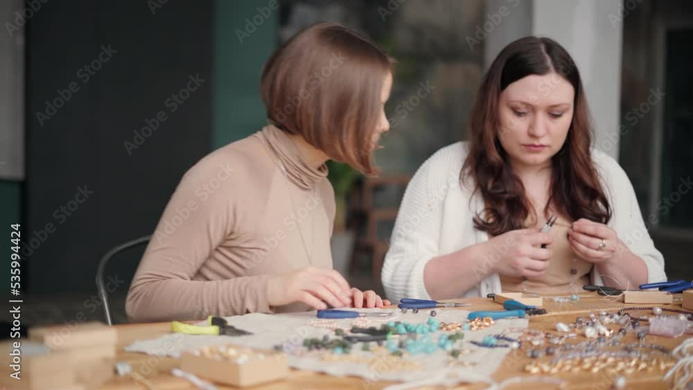 Two jewelry designers working in studio with tools making gemstone necklaces, bracelets and earrings. Female friends crafting jewellery together Two jewelry designers working in studio with tools making gemstone necklaces, bracelets and earrings. Female friends crafting jewellery together