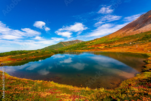 秋の北海道・大雪山の旭岳で見た、山頂近くの池周辺に広がる色鮮やかな紅葉と快晴の青空 © 和紀 神谷