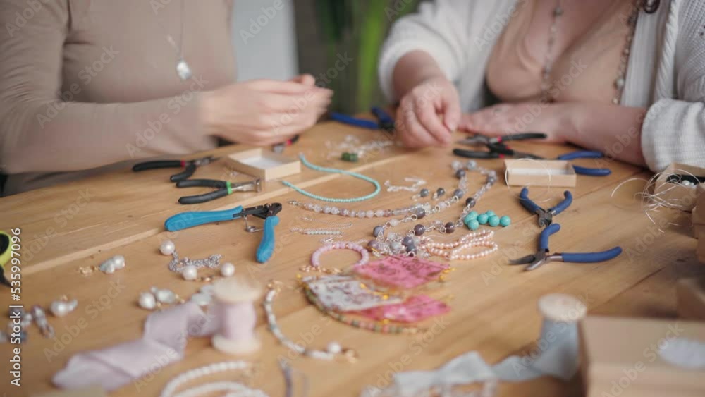 Two jewelry designers working in studio with tools and different gemstones making necklaces, bracelets and earrings. Female friends crafting jewellery together Two jewelry designers working in studio with tools and different gemstones making necklaces, bracelets and earrings. Female friends crafting jewellery together