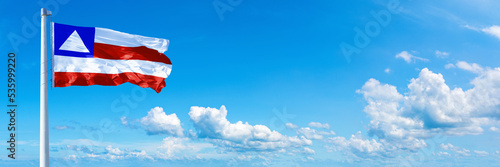 Bahia - state of Brazil, flag waving on a blue sky in beautiful clouds - Horizontal banner