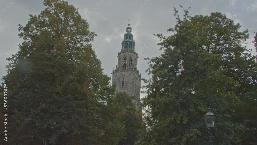 Tilt down of Martini tower in Groningen, the Netherlands behind green trees in a park Tilt down of Martini tower in Groningen, the Netherlands behind green trees in a park