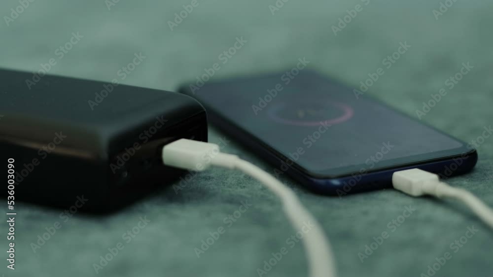 Charging a smartphone using a portable power bank charger, close-up. Low battery level in the phone. Charging a smartphone using a portable power bank charger, close-up. Low battery level in the phone.
