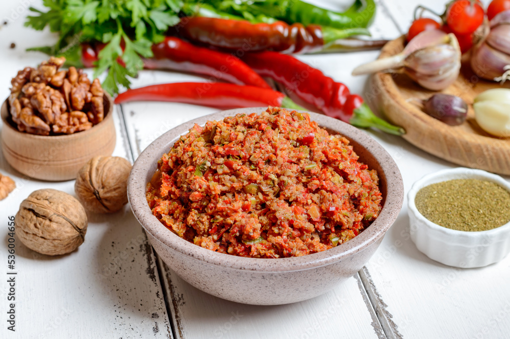 Adjika in a bowl and ingredients on a white wooden table. Georgian cuisine, spicy hot pepper sauce. Adjika in a bowl and ingredients on a white wooden table. Georgian cuisine, spicy hot pepper sauce.