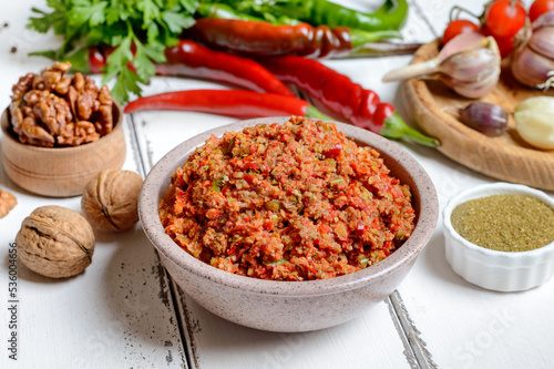 Adjika in a bowl and ingredients on a white wooden table. Georgian cuisine, spicy hot pepper sauce.