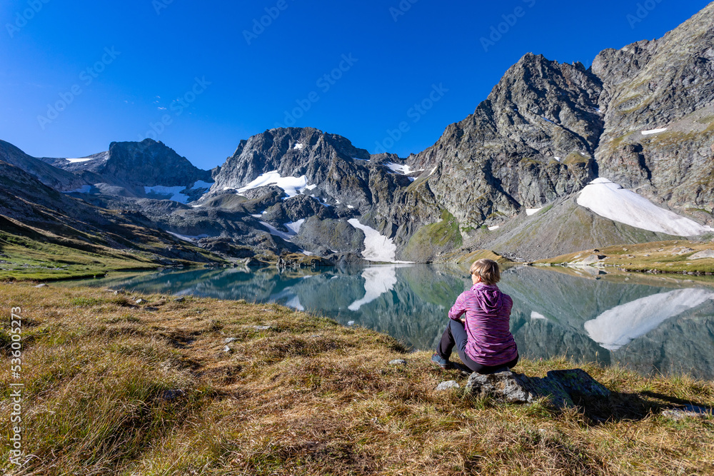 The girl sits against the backdrop of mountain peaks and a blue lake. Beautiful mountain landscape for vacation, travel and healthy lifestyle