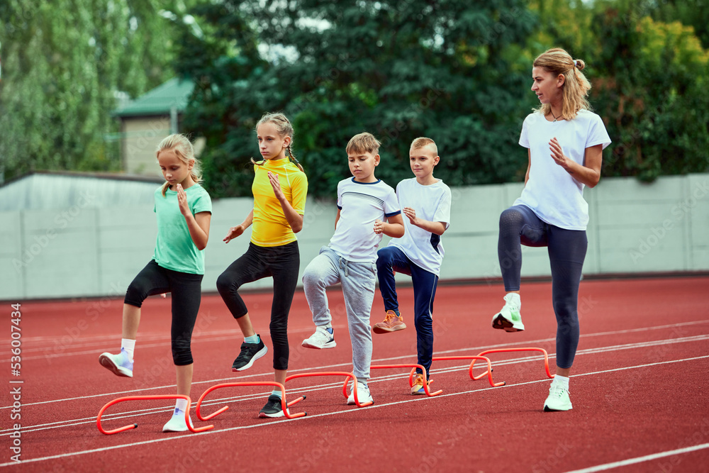 Female coach training athletes. Group of children running on treadmill at the stadium. Concept of sport, achievements, studying, goals, skills. Little boys and girls training outdoor.