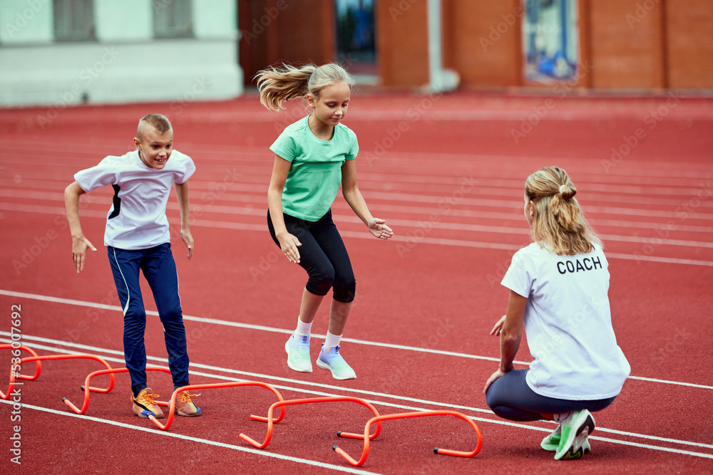 Female coach training athletes. Group of children running on treadmill at the stadium. Concept of sport, achievements, studying, goals, skills. Little boys and girls training outdoor.