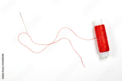 Needle with red thread and spool of thread on a white background