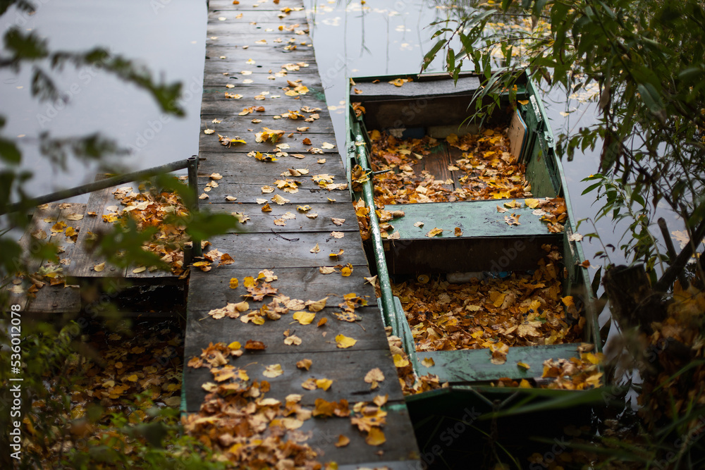 old wooden fishing green boat stands at the pier on the lake in the village of autumn in cloudy weather. old wooden fishing green boat stands at the pier on the lake in the village of autumn in cloudy weather.