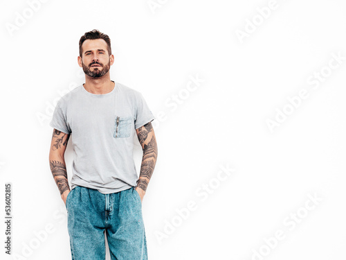 Portrait of handsome confident stylish hipster lambersexual model. Sexy man dressed in T-shirt and jeans. Fashion male isolated on white wall in studio © halayalex