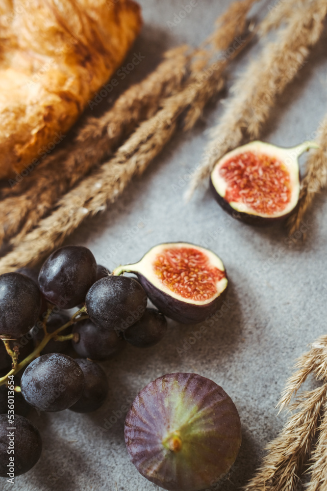 Autumn attributes. Croissant, dark grapes and figs on the grey table Autumn attributes. Croissant, dark grapes and figs on the grey table