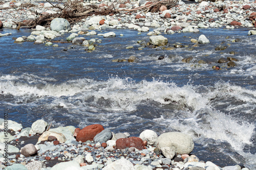White water of the  mountain stream in summer time. Torrent waves, white and brown stones, green grass on the bank