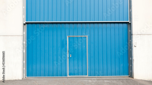 Puerta metálica azul en nave industrial de hormigón 