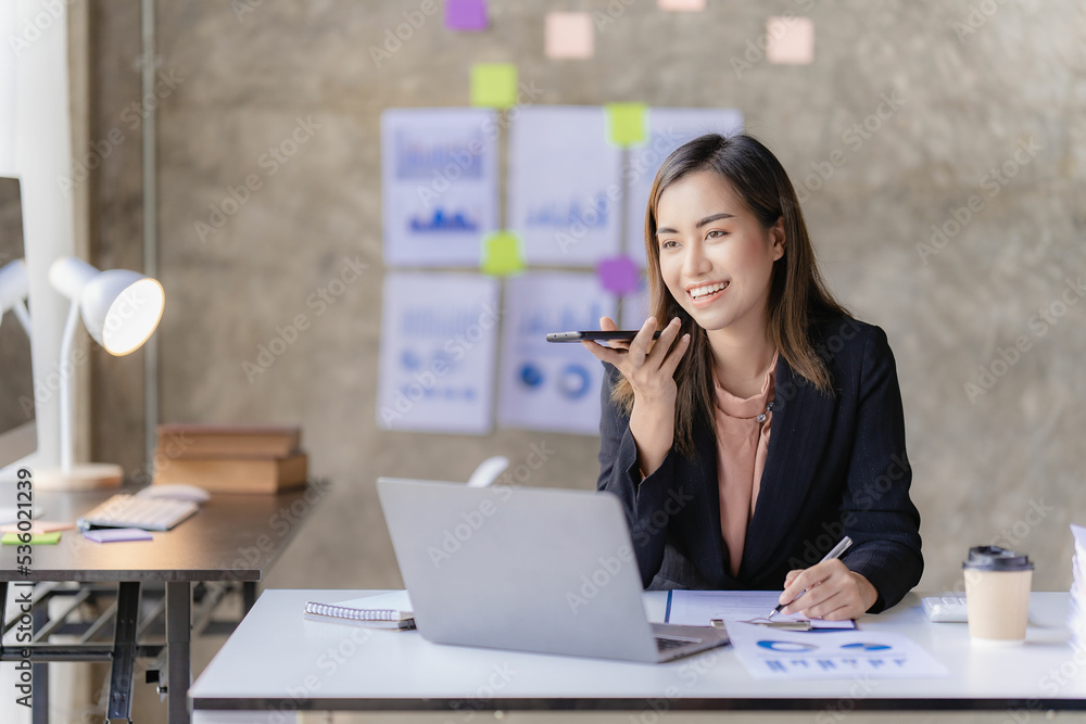 Asian businesswoman holding smartphone with charts or documents at work using business laptop calculator financial accountant calculating money Asian businesswoman holding smartphone with charts or documents at work using business laptop calculator financial accountant calculating money
