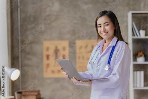 Photography Asian female doctor sitting at a hospital desk, giving health care and disease prevention advice, convenient online services to patients and smiling, writing prescriptions to order medicine
