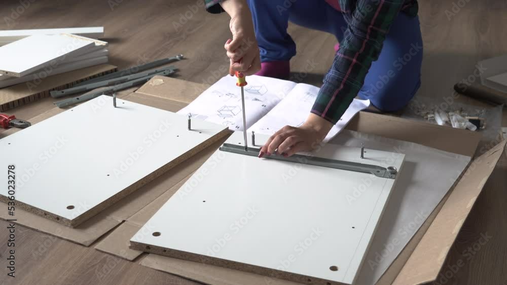 Woman screwing screw while assembling furniture on the floor of apartment Woman screwing screw while assembling furniture on the floor of apartment