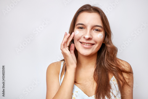 A beautiful girl applies moisturizing cream to her face.