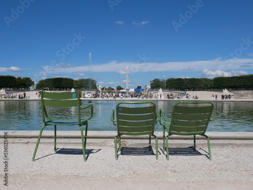 Paris, France: back view of three green iron garden chairs near the Octagonal Basin fountain in Tuileries Garden, Paris. Place de la Concorde Luxor Obelisk in the background.