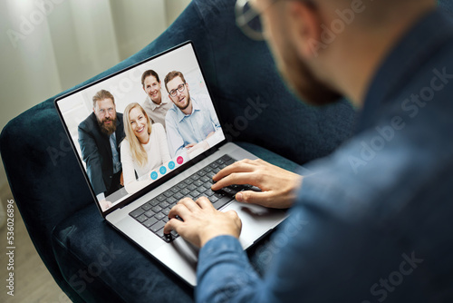 Young man in denim jacket has conversation using video chat on laptop, team of young business people connecting through internet