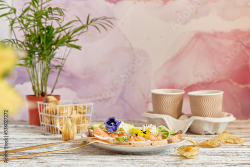 Aesthetic lunch time - appetizer toasts with smoked salmon, avocado, arugula, cucumber and edible flowers. Cardboard cups with coffee. Cozy lagom home