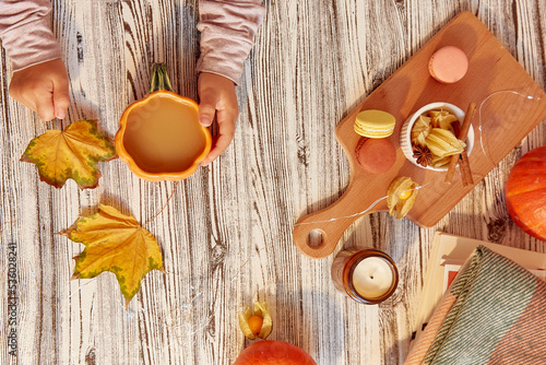 Autumn composition - child holding a cup of cocoa and autumn leaves. Macaroons, winter cherry, pumpkin and candle. Autunn lagom aesthetics photo