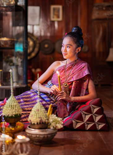Portrait photo of a young beautiful asian Laos lady wearing traditional Lao costume dresses with flower bouquet and candles prepared for Loy Krathong festival sitting on the floor with a elegant pose