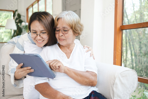 An Asian woman teaches an elderly woman who is her mother, to use a tablet. Using technology of seniors at home concept.