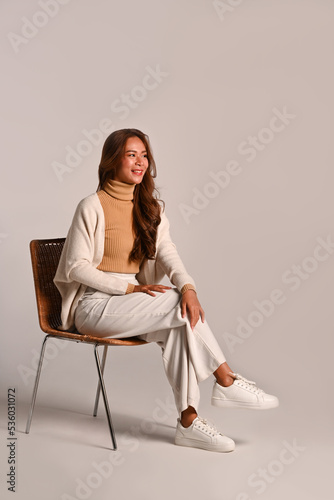 Full length portrait of beautiful woman wearing warm sweater sitting on a chair over white background. Studio shot