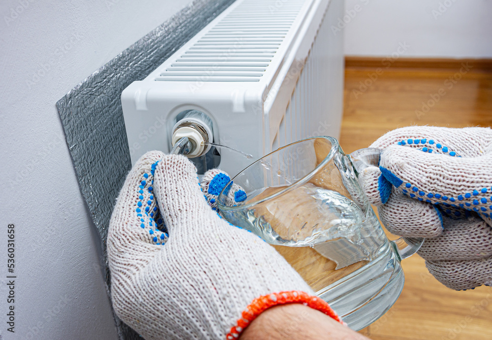 Bleed valve in heating radiator. Hand with a key for draining air drains  water and air