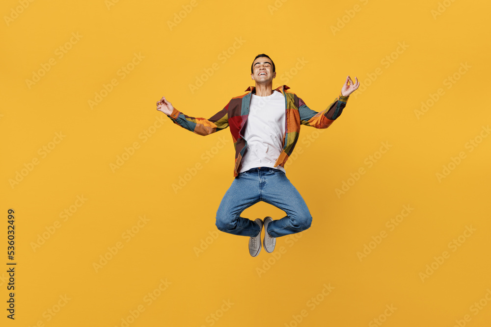 Full body young spiritual middle eastern man wear casual shirt white t-shirt jump high hold spreading hands in yoga om aum gesture relax meditate try to calm down isolated on plain yellow background.