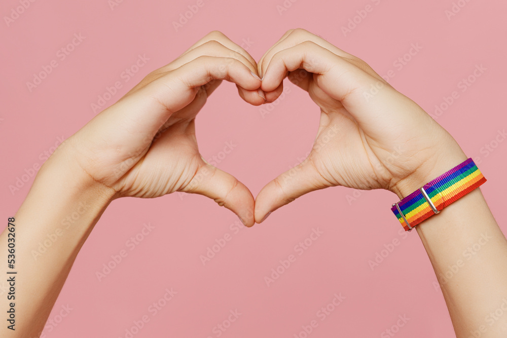 Fototapeta premium Close up cropped gay male hand with bracelet show shape heart with hands heart-shape sign isolated on pastel plain light pink background. Lifestyle lgbtq pride concept. Copy space advertising mock up.